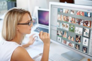 Attractive blonde sitting in the office looking at pictures on computer monitor